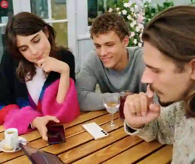 Drei Personen sitzen an einem Gartentisch und schauen auf ein Smartphone